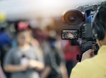 Video camera man working outdoors with young woman reporter.