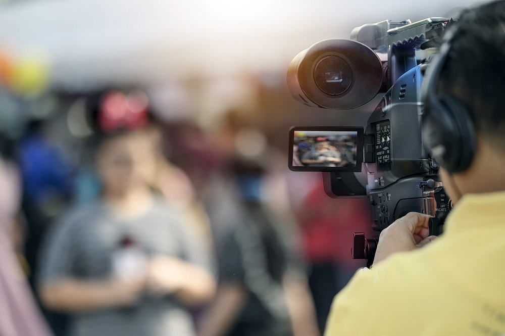 Video camera man working outdoors with young woman reporter.