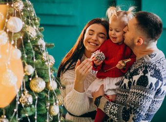 Family with little daughter hanging toys on Christmas tree