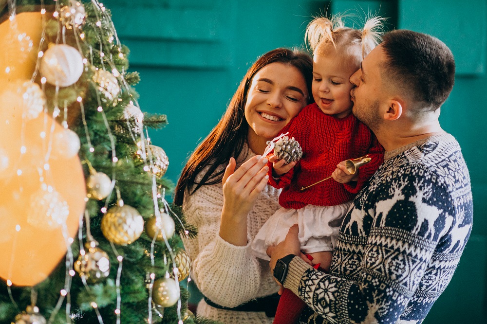 Family with little daughter hanging toys on Christmas tree