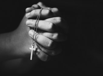 Hands holding cross while praying.