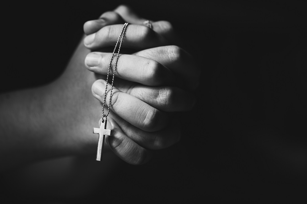Hands holding cross while praying.