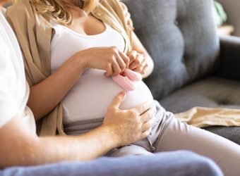 Future mother applying baby girl shoes to belly