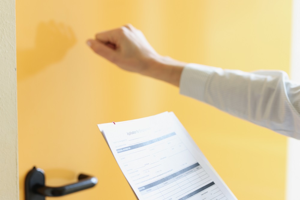 Woman holds application form in her hand and knocks on door